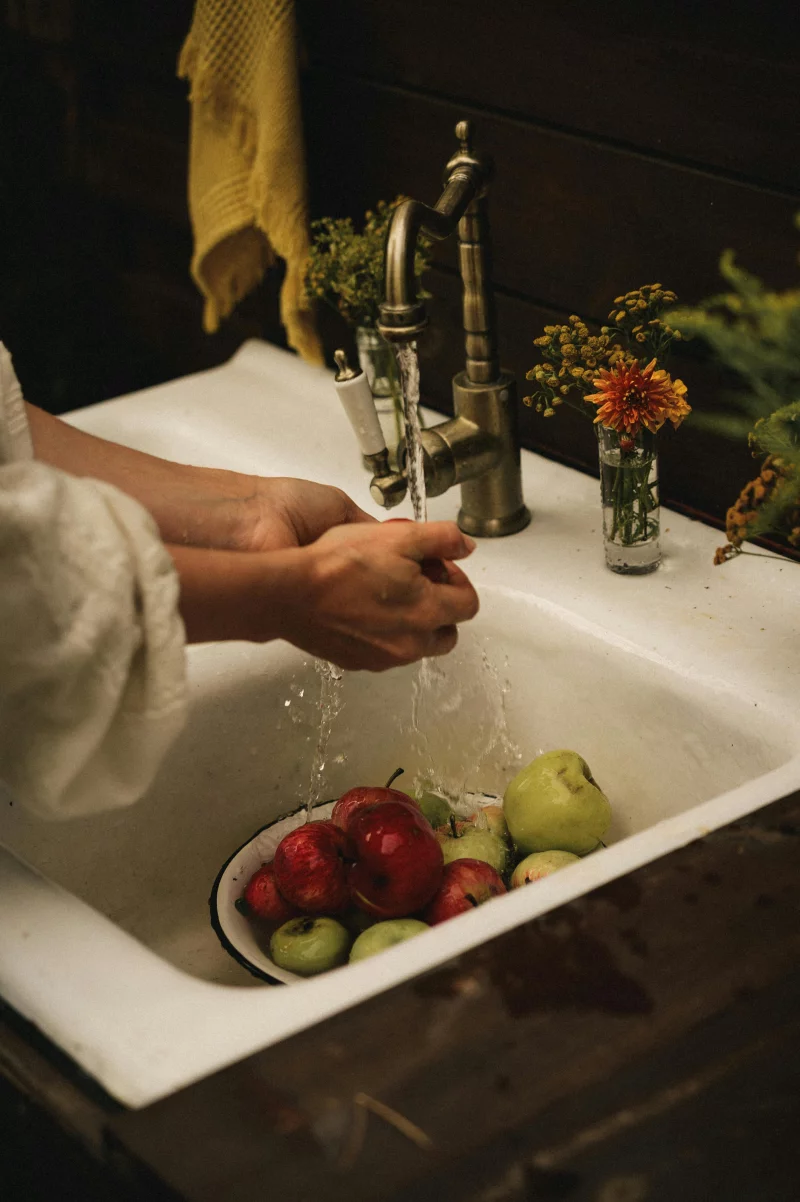 Hands washing apples in a vintage sink with rustic decor, evoking a homely autumn feel.