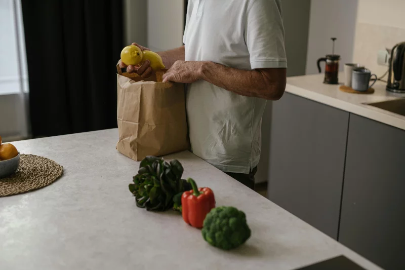 A person organizes fresh fruits and vegetables in a modern kitchen setting.