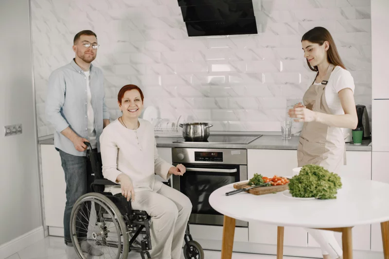 Three adults enjoying family time preparing food in a bright kitchen.