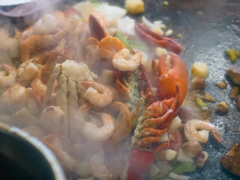 Steaming fresh seafood including shrimp and lobster grilling on a hot plate with vegetables.