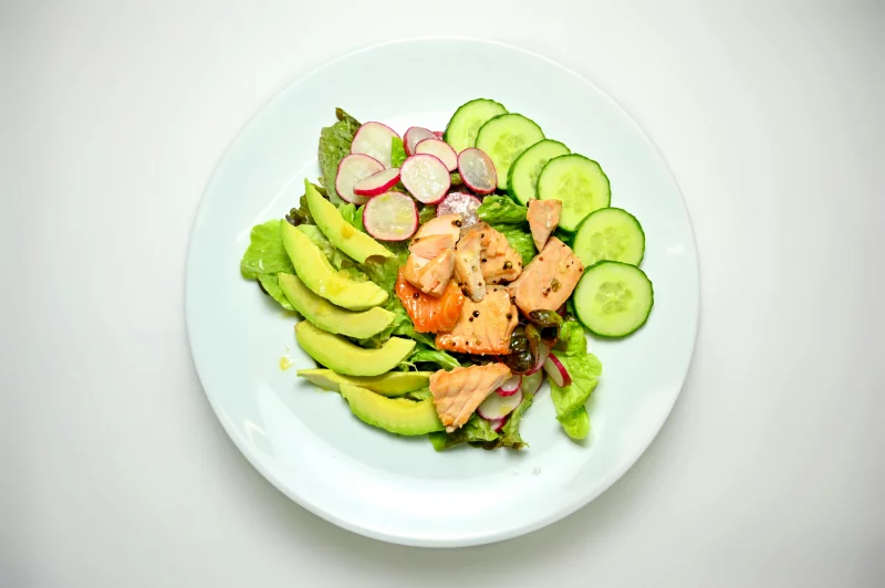 A delicious and healthy mixed salad with salmon, avocado, and vegetables on a white plate.