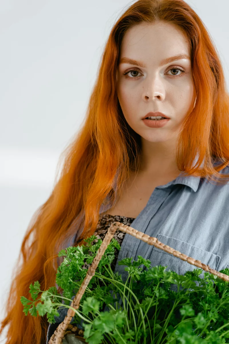 A red-haired woman holding a basket of fresh parsley, captured in a studio setting.