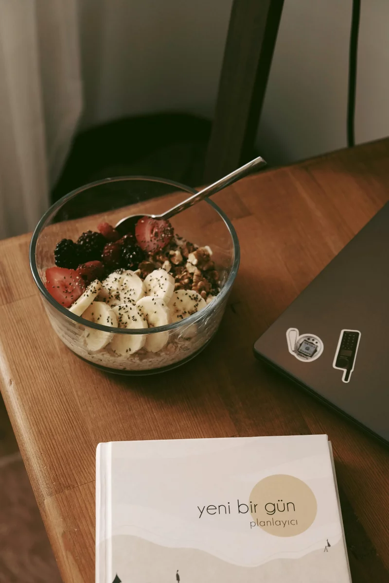 Delicious bowl of fresh fruits and granola with a notebook and laptop on a desk.