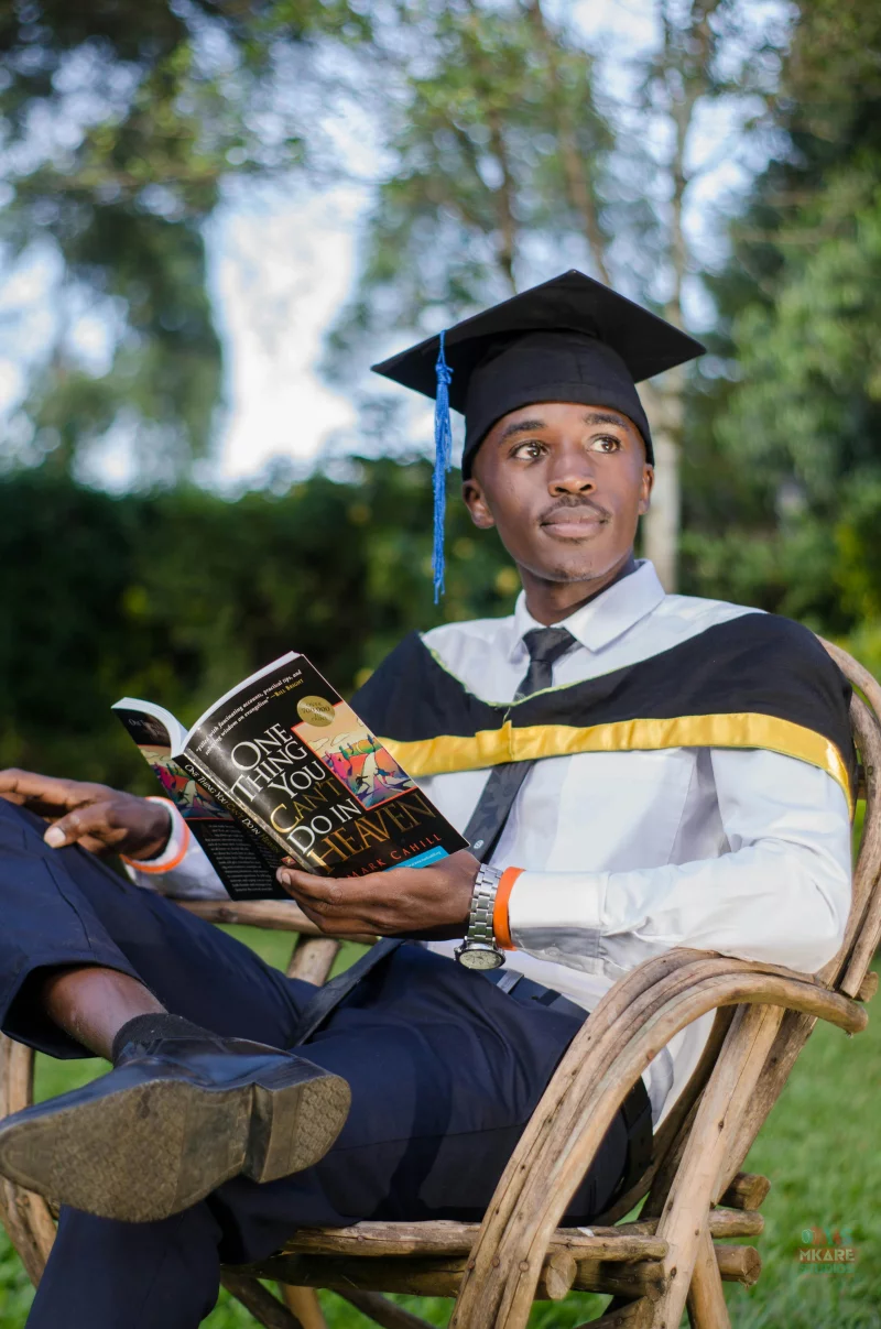Graduation day moment with young man in cap and gown reading outdoors