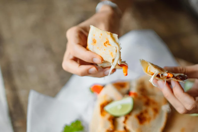 Close-up of hands enjoying a cheese and vegetable tortilla with lime.