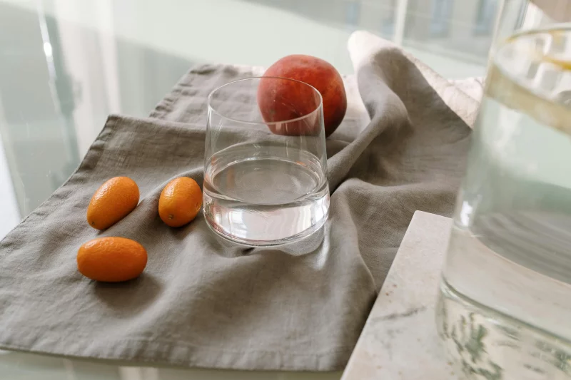 Aesthetic arrangement of kumquats and a peach beside a water glass on a table.