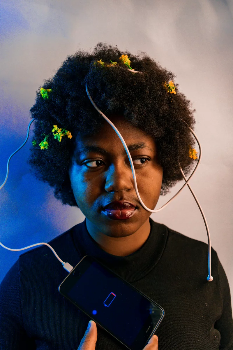 Unique artistic portrait depicting a woman with flowers in hair, holding smartphone with low battery.