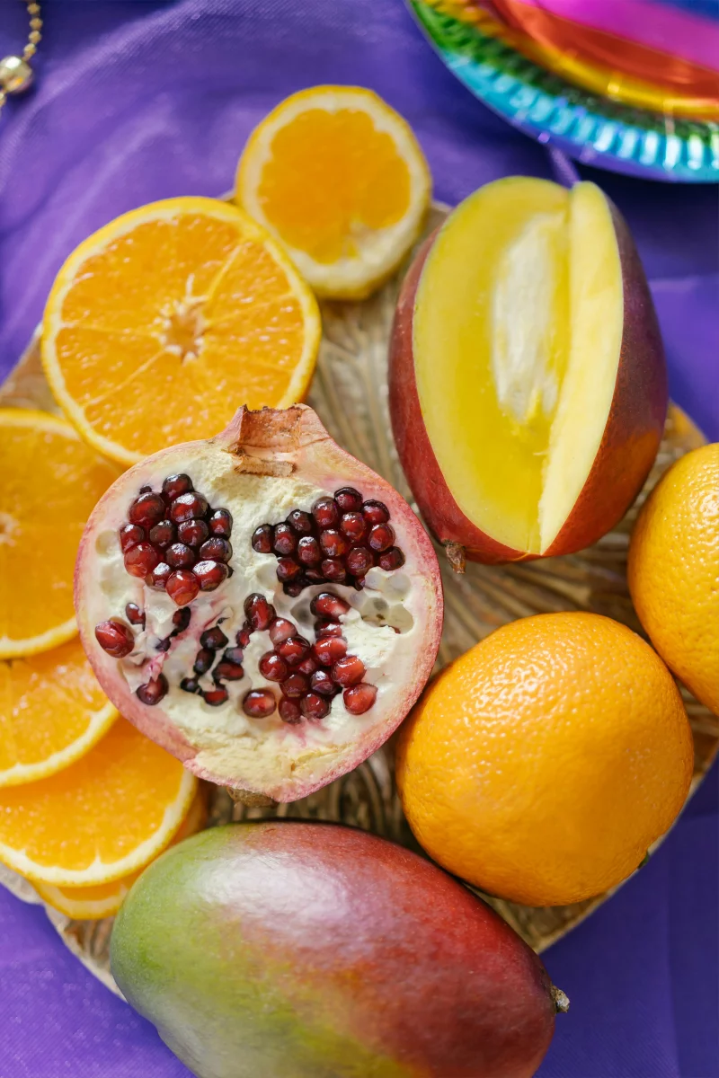 Colorful assortment of sliced tropical fruits on a purple background, including mango, orange, and pomegranate.