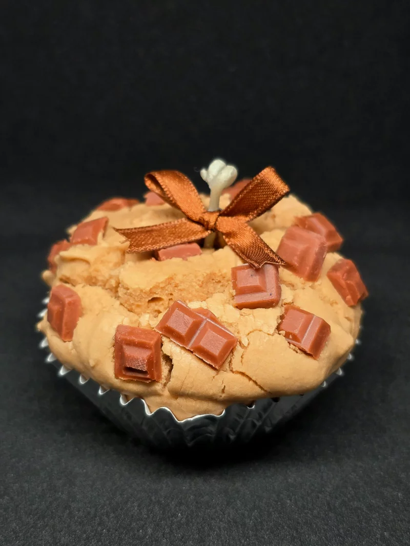 A close-up of a cupcake topped with chocolate chunks and a decorative ribbon.