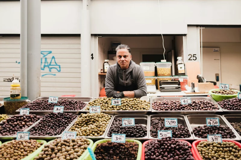 Market scene featuring a seller with an array of olives, showcasing urban culture.
