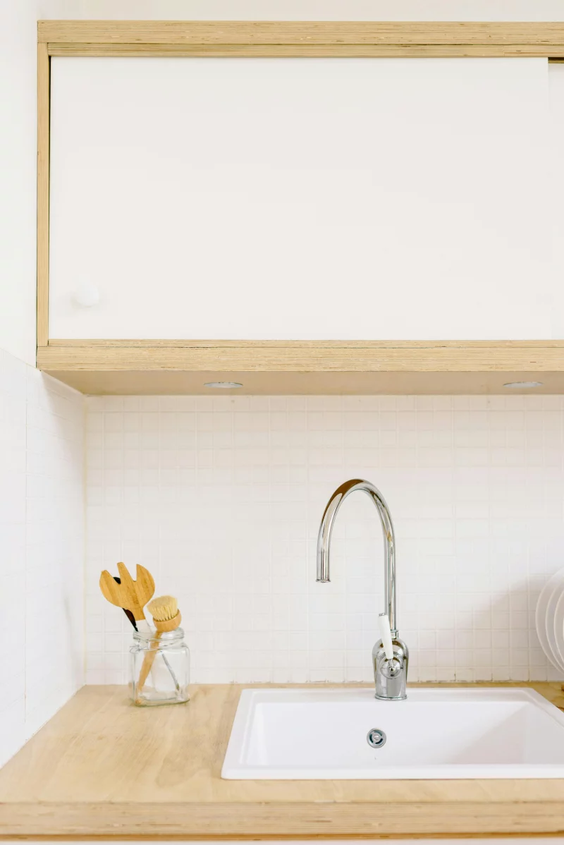 A clean, minimalist kitchen setup featuring a sink with wooden cabinets and modern fixtures.