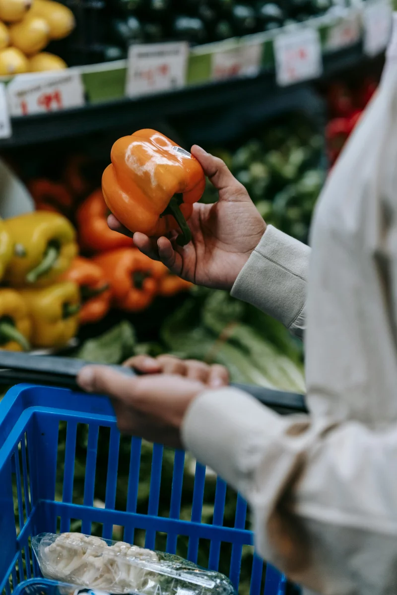 Close-up of a person choosing a bell pepper in a grocery store, focusing on healthy food choices.