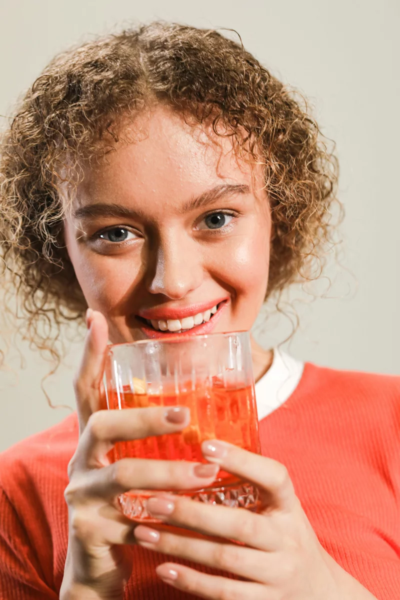 Smiling young woman holding a refreshing beverage in a close-up portrait.