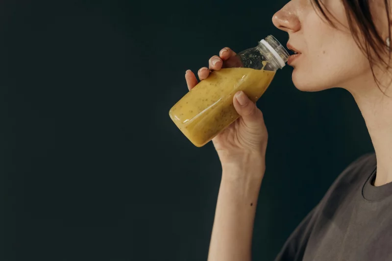 Side profile of a young woman sipping a nutritious smoothie from a bottle, showcasing a healthy lifestyle.