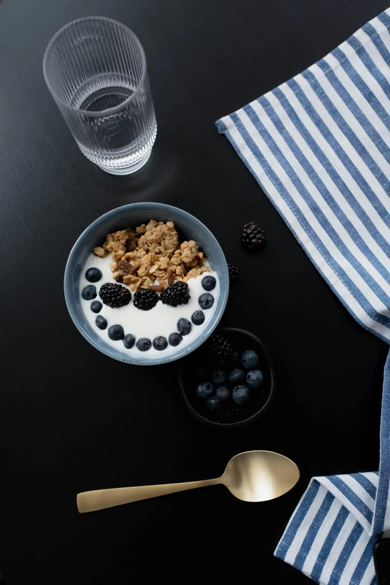 A healthy breakfast bowl with granola, blackberries, and blueberries on a dark surface.