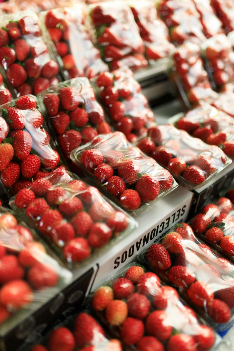 Fresh strawberries in transparent plastic packaging displayed in a market setting.