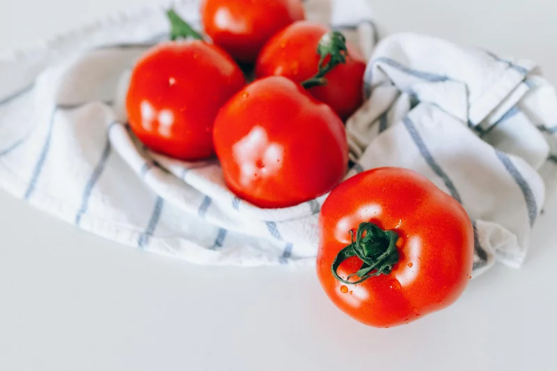 Close-up of fresh red tomatoes resting on a white and blue striped cloth.