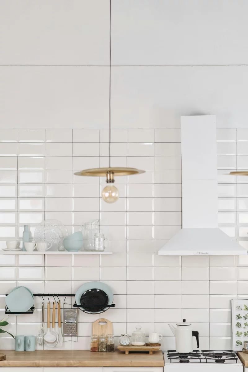Bright and modern kitchen with white tiles, shelves, and a stylish light fixture.
