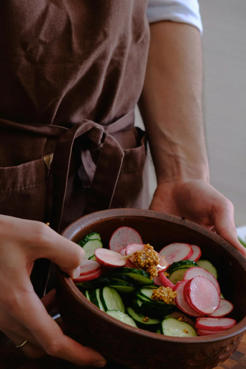 Chef holding a bowl of fresh vegetable salad with radishes and cucumbers.