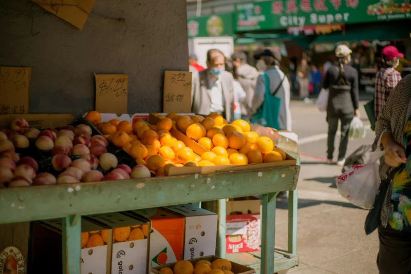 Colorful street market scene with fresh fruits and urban shoppers outdoors.