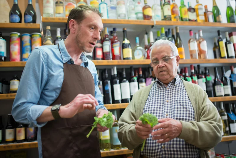 Senior man and store clerk examine fresh lettuce in a Portuguese grocery store.