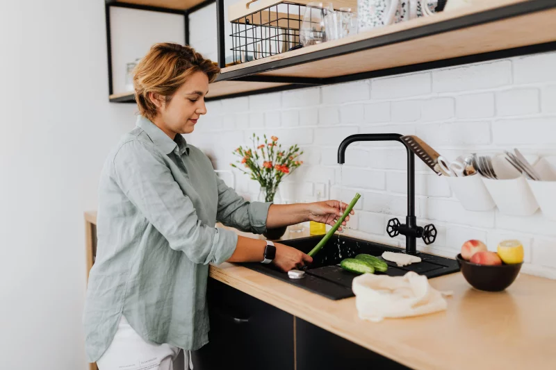 A woman washing vegetables in a stylish kitchen with contemporary decor.