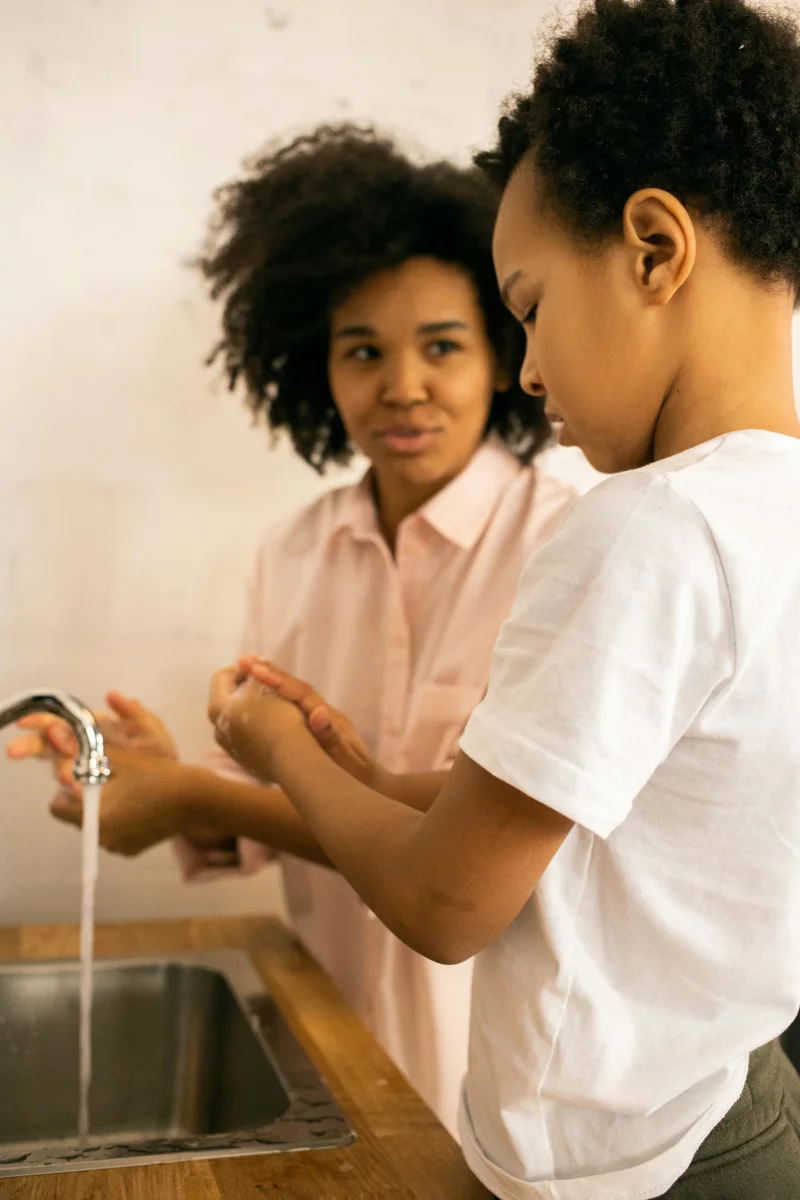 A mom and son washing hands together in a kitchen for hygiene and bonding.