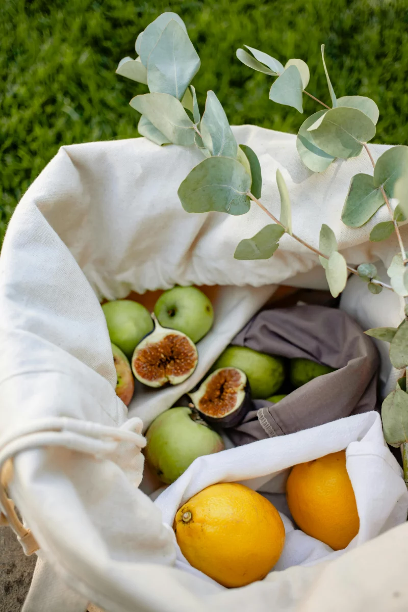 A reusable basket with fresh fruits and eucalyptus, promoting sustainable living.