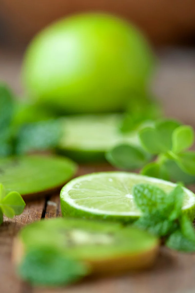 Close-up of sliced limes with fresh mint leaves on rustic wood, showcasing vibrant green tones.