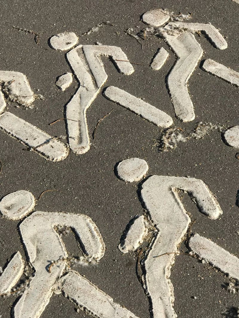 Close-up of white pedestrian symbols on a rough asphalt city pathway.