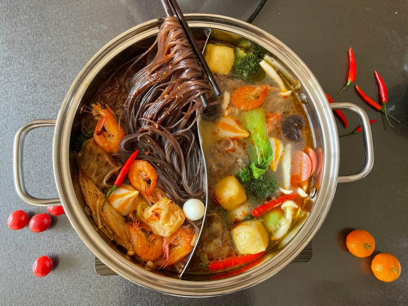 Top view of a vibrant hot pot with noodles, shrimp, and vegetables.