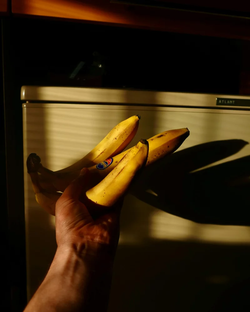 A hand holding bananas casts a shadow against a fridge, creating a striking contrast.
