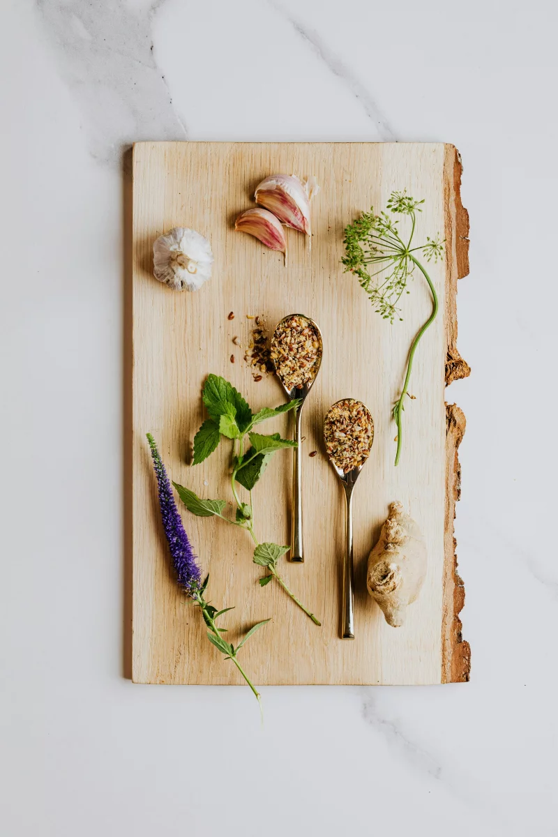 Flat lay of assorted spices, herbs, garlic, and ginger on a wooden board for culinary use.