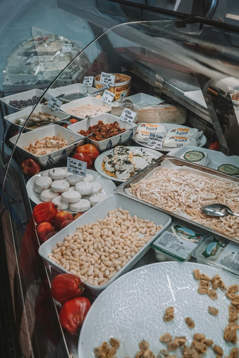 A display of assorted cheeses, fresh pasta, and vegetables in an Italian deli counter, offering a taste of Turin.