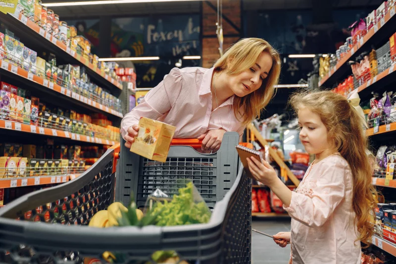 A mother and her daughter shopping together in a supermarket, browsing items.