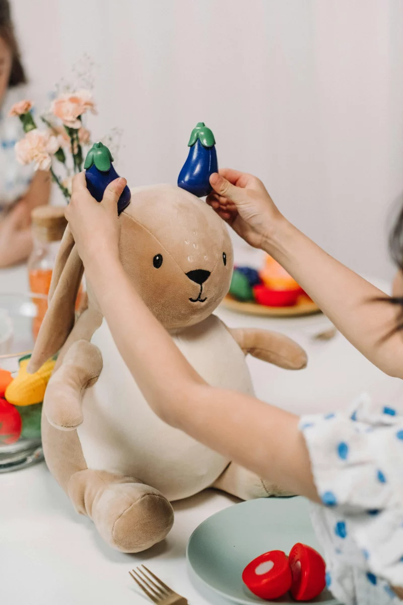 A child plays with a stuffed rabbit and toy vegetables indoors.