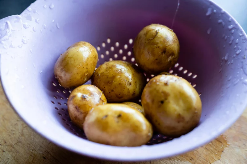 Close-up of fresh potatoes in a purple colander with water droplets.