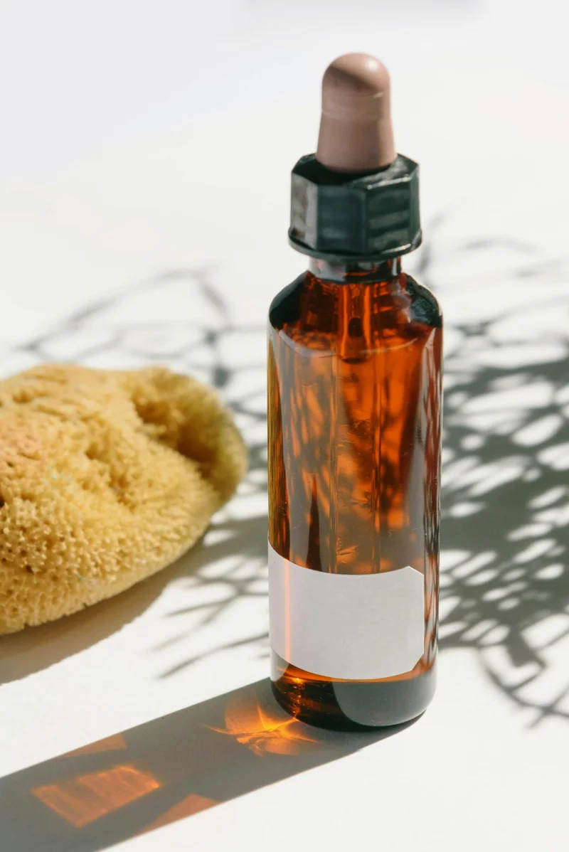 Amber glass dropper bottle with sponge, casting shadows on a light surface, ideal for skincare use.