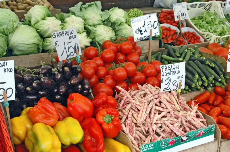 Colorful variety of fresh vegetables displayed at an outdoor market stall with price signs.