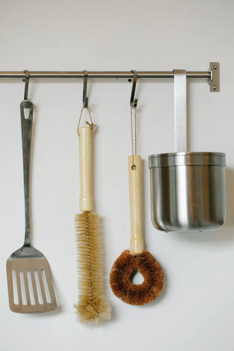 Diverse kitchen utensils including brush and stainless tools on wall hanger.