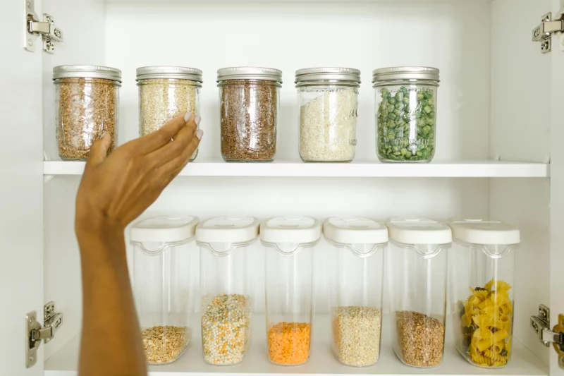 A neat pantry shelf showing various grains stored in labeled glass and plastic containers, promoting kitchen organization.