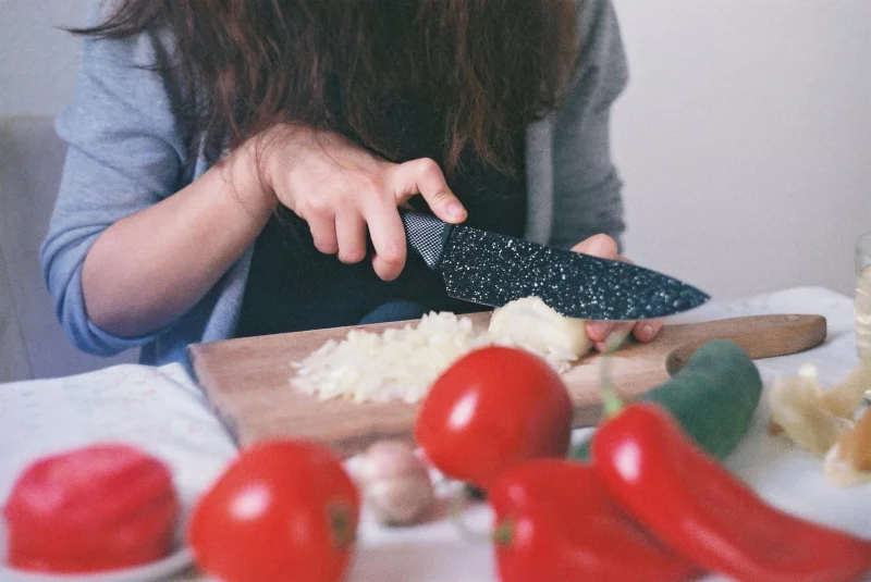 Close-up of a woman dicing onions and tomatoes on a wooden cutting board in a kitchen setting.