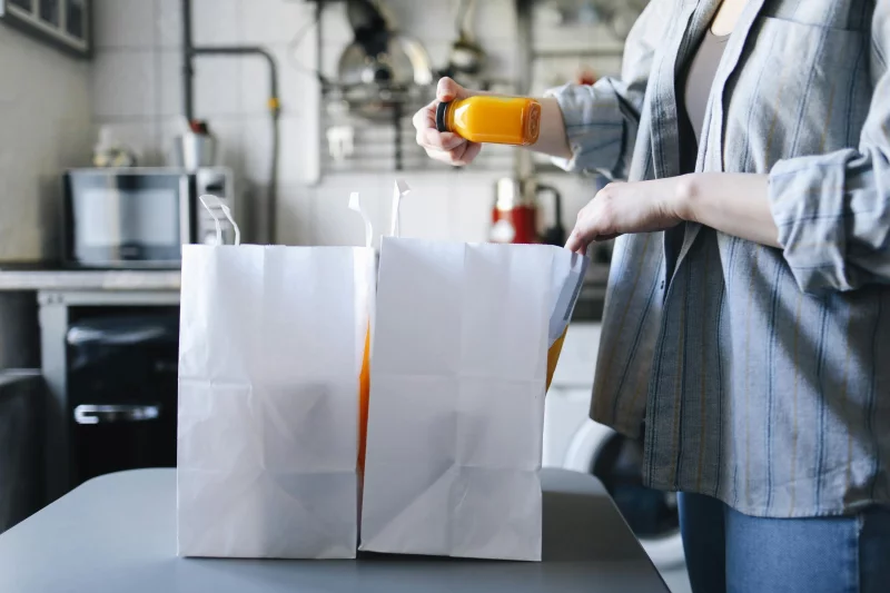 A woman unpacking groceries from paper bags on a kitchen table.
