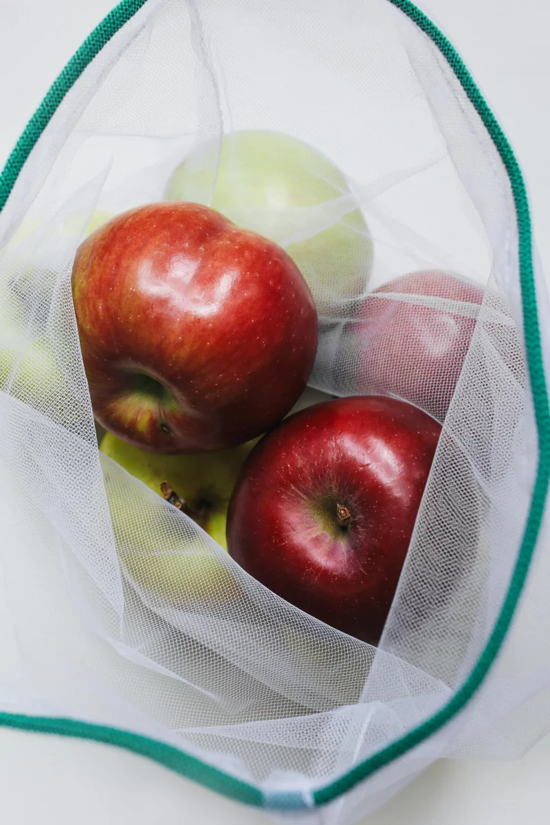 Close-up of fresh red apples in a reusable mesh bag against a white background.