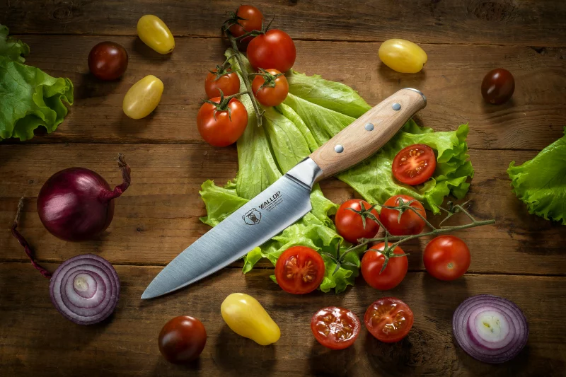 Flat lay of fresh vegetables and a kitchen knife on a rustic wooden surface, ideal for culinary themes.
