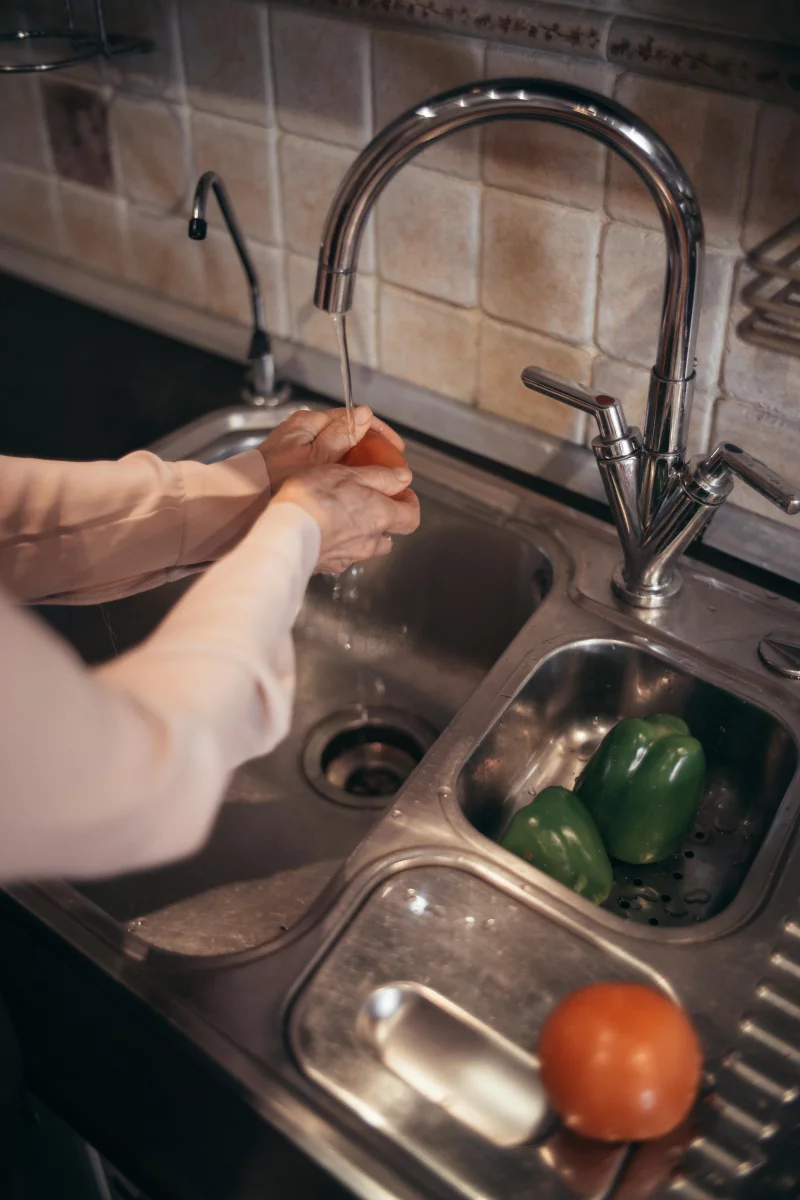 Person washing fresh vegetables under running tap water in a kitchen.