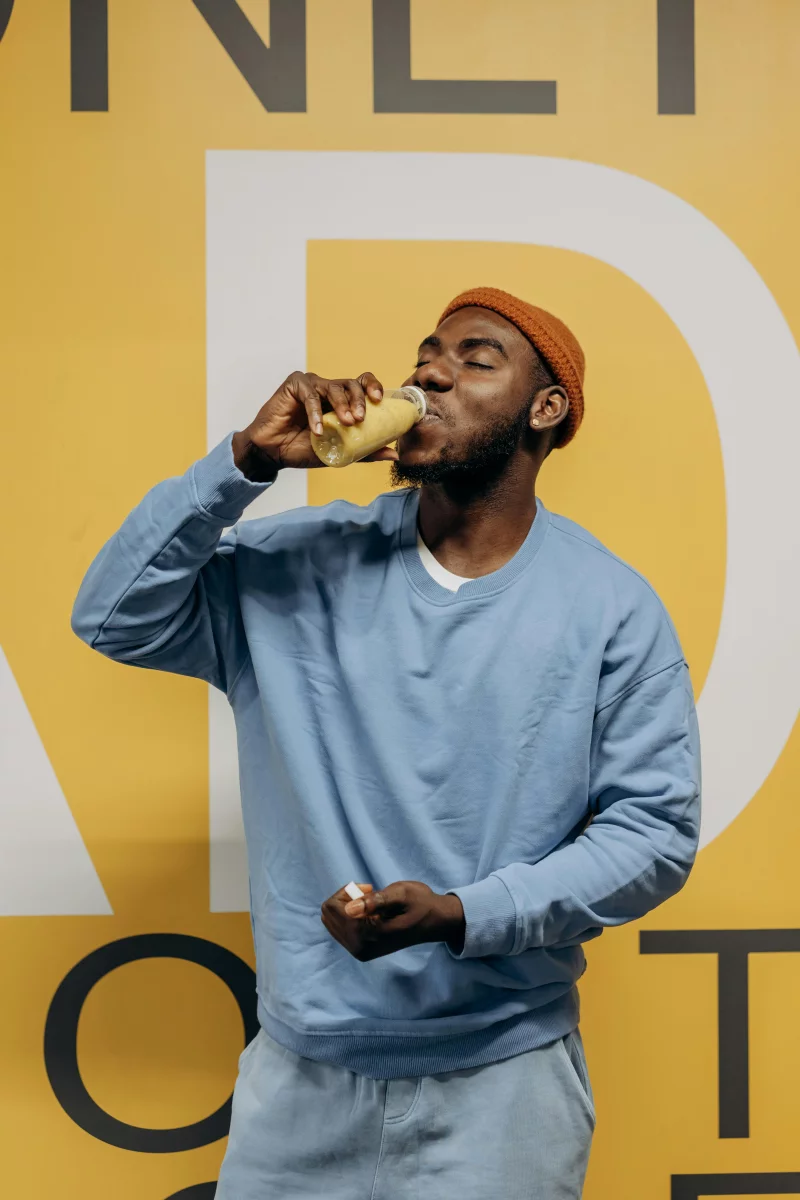 Casual man in blue sweatshirt drinking healthy juice with a cheerful expression.