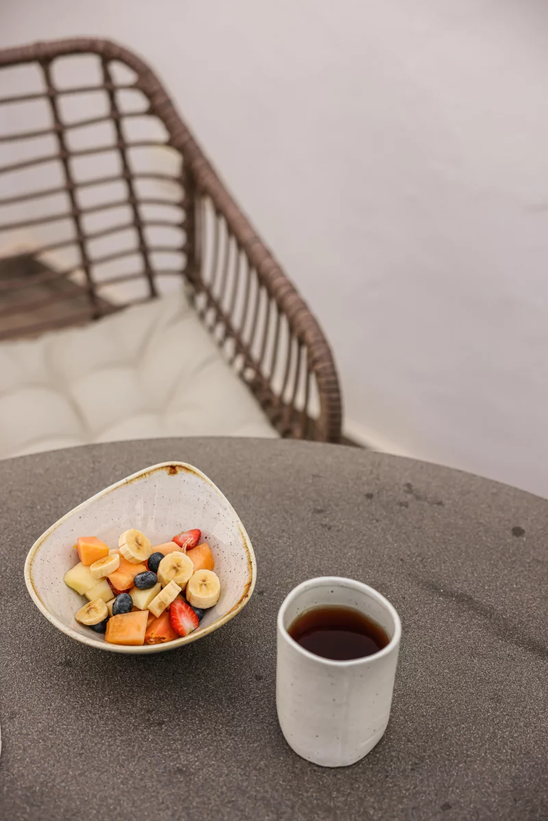 A nutritious breakfast setup featuring a fruit bowl beside a hot cup of coffee on a stylish table.