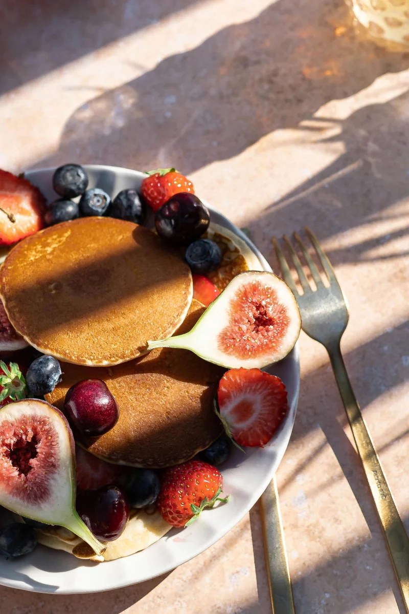 A mouthwatering stack of pancakes with figs, strawberries, blueberries, and cherries, perfect for brunch.