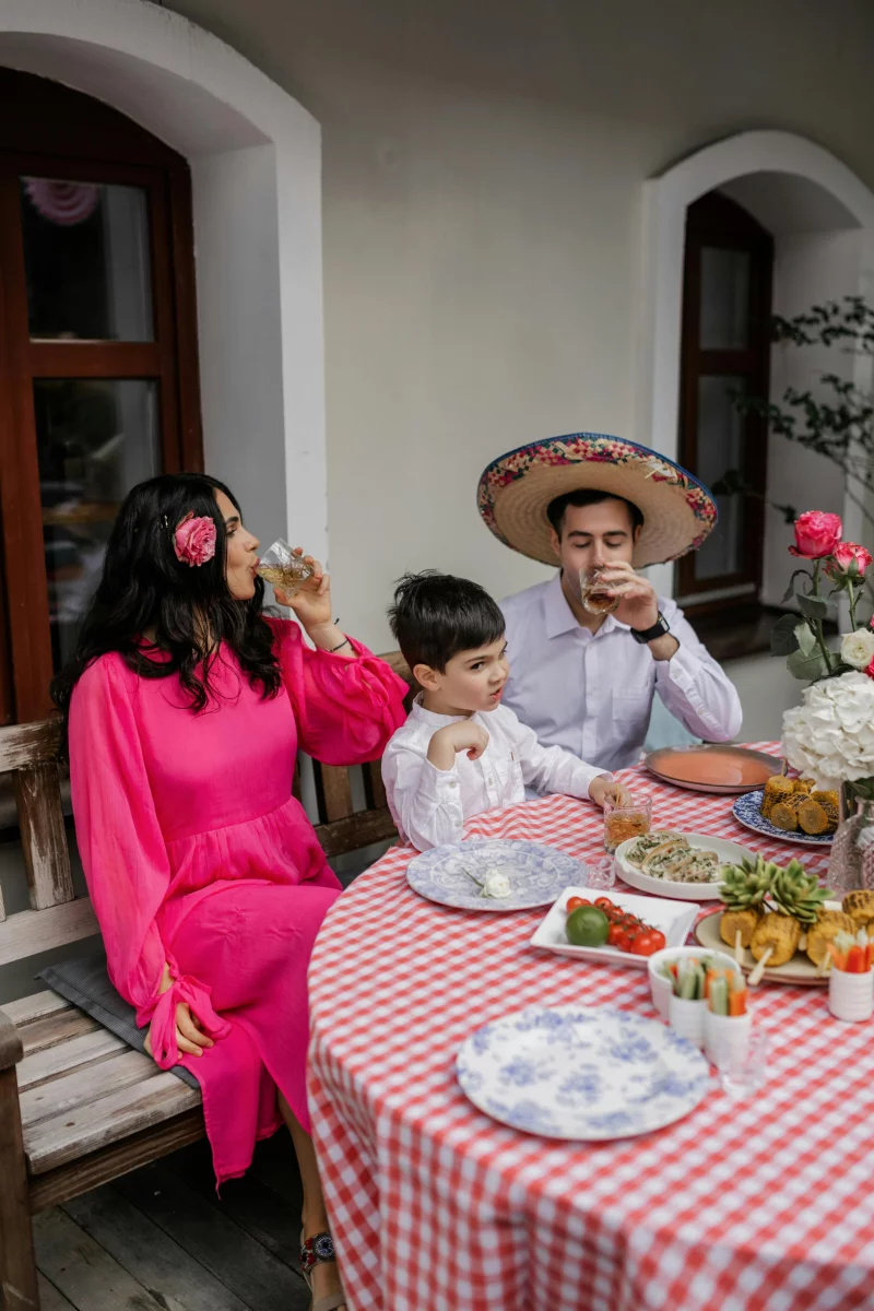 A family enjoys a festive meal at a table with vibrant decorations and traditional Mexican attire.